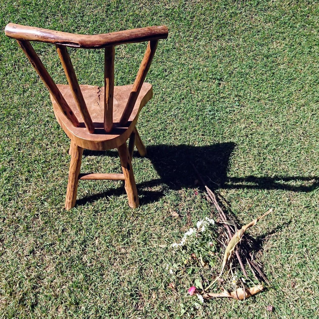 Cadeira de madeira, feita à mão, no gramado, com uma pequena oferenda no chão