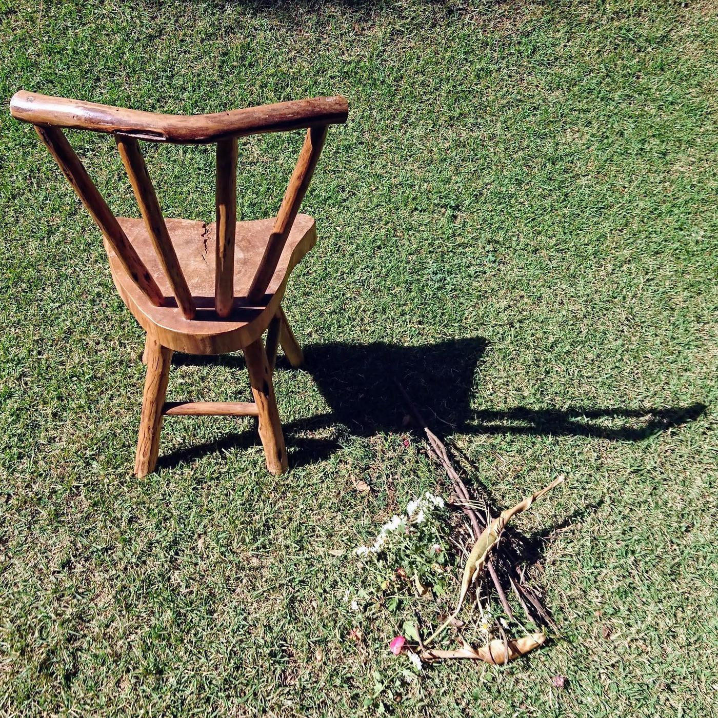 Cadeira de madeira, feita à mão, no gramado, com uma pequena oferenda no chão